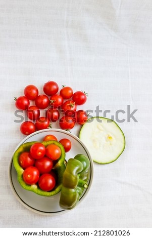 Small tomatoes in cut green pepper with zucchini slice at white linen background. Vertical image