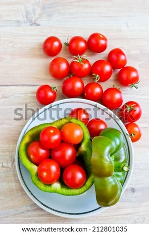 Small tomatoes in cut green pepper on white dish at wooden background. Vertical image