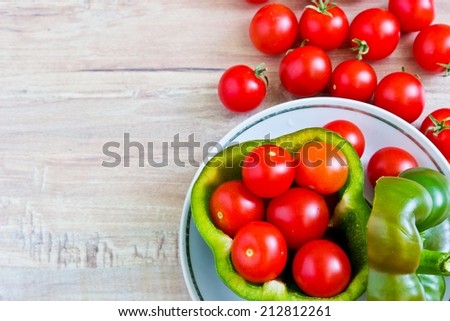 Small tomatoes in cut green pepper on white dish close up at wooden background. Horizontal image. Objects at the right part of image
