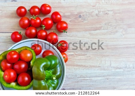 Small tomatoes in cut green pepper on white dish close up at wooden background. Horizontal image. Objects at the left part of image