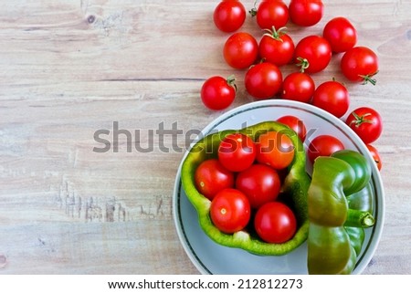 Small tomatoes in cut green pepper on white dish close up at wooden background. Horizontal image. Objects at the right part of image