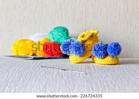 Colorful wool baby bootees with wool and knitting needles on white background