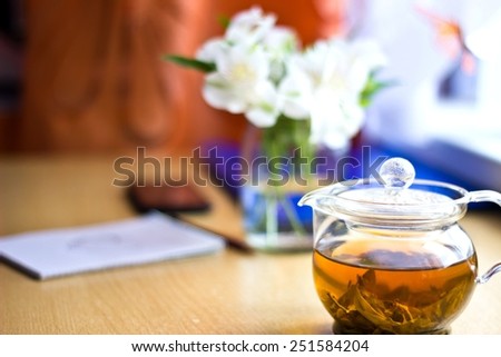 Celebrating composition: bouquet of white freesia flowers, smartphone, pen, teapot and notebook with painted heart. Selective focus on teapot. Horizontal image with multicolored bokeh background