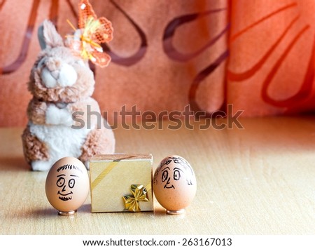 Painted easter eggs with man and woman smiling faces. Eggs on wedding rings near golden gift box. Blurred background with easter bunny. Conceptual funny image. Focus on eggs