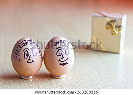Painted easter eggs with man and woman smiling faces. On wedding rings. Blurred background with golden gift box. Conceptual funny image. Focus on eggs