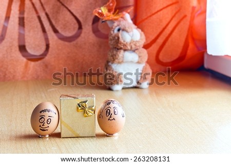 Painted easter eggs with man and woman smiling faces. Eggs on wedding rings near golden gift box. Blurred background with easter bunny. Conceptual funny image. Focus on eggs