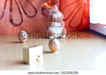 Painted easter eggs with man and woman smiling faces. Eggs on wedding rings. Blurred background with golden gift box and easter bunny. Conceptual funny image. Focus on man egg