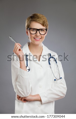 Portrait of a female doctor pointing with pen. Waist up studio shot on gray background.