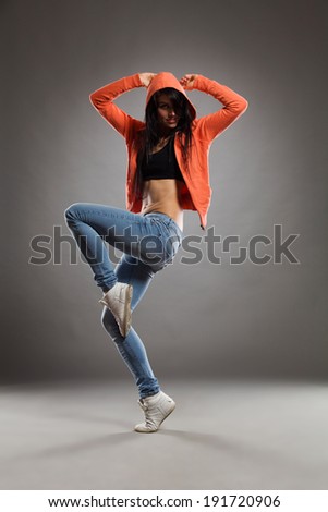 Female dancer posing on one leg and arms raised. Full length studio shot on gray background.