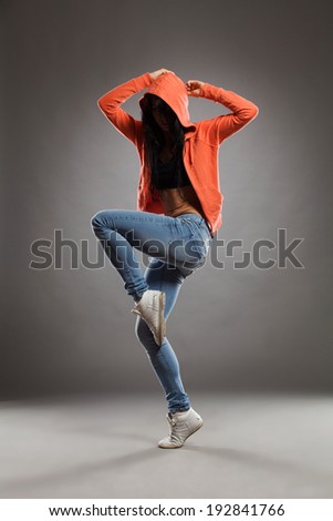 Female dancer in hood posing on one leg. Full length studio shot on gray background.