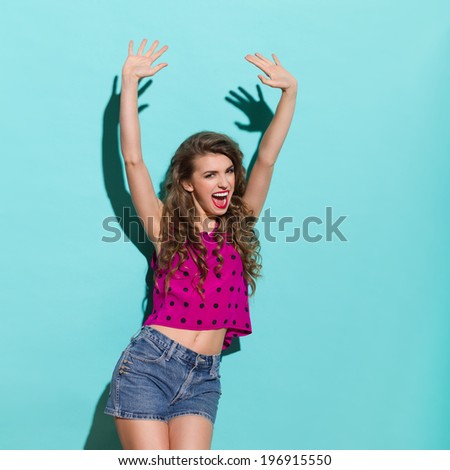 Cheering girl. Beautiful woman shouting with arms outstretched. Three quarter length studio shot on teal background.