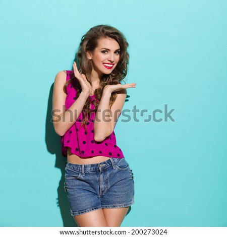 Smiling beautiful young woman posing in the sunlight. Three quarter length studio shot on teal background.