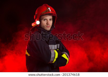 The fireman. Firefighter in red helmet standing with arms crossed. Waist up studio shot on black background.