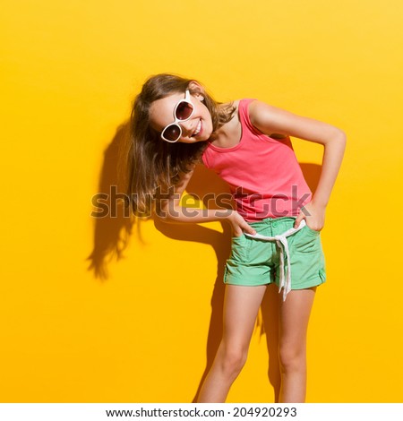 Laughing girl in sunlight. Three quarter length studio shot on yellow background.