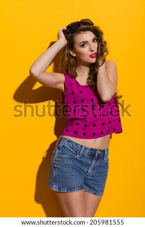 Beautiful young woman posing with hands in hair. Three quarter length studio shot on yellow background.