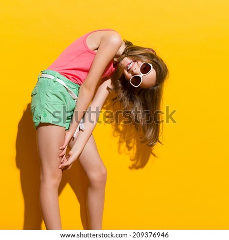 Playful and smiling girl in the sunlight. Three quarter length studio shot on yellow background.