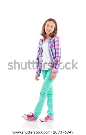 Cheerful little girl posing in lumberjack shirt and green trousers. Full length studio shot isolated on white.
