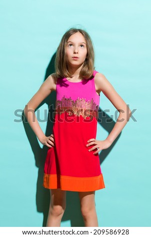 Surprised elegance little girl looking up. Three quarter length studio shot on teal background.