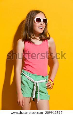 Little girl in sunglasses posing in the sunlight. Three quarter length studio shot on yellow background.