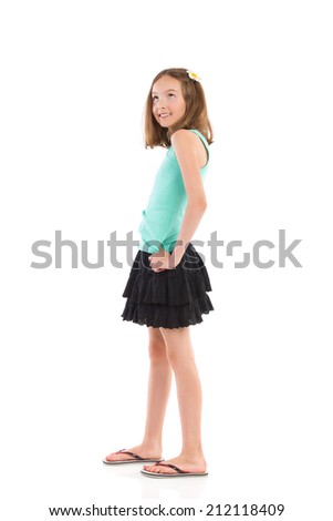 Young girl in teal shirt and black skirt posing with flower in her hair and looking up. Full length studio shot isolated on white.
