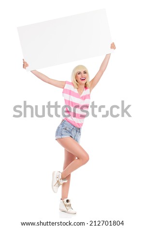 Message for you. Laughing blond woman standing on one leg and holding a blank placard over her head. Full length studio shot isolated on white.