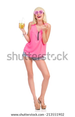 Flirting at the party. Blonde young woman in high heels, pink top and jeans shorts holding lime drink and beckoning. Full length studio shot isolated on white.