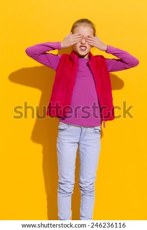 I don\'t want to see it. Young blond girl closes her eyes with hands. Three quarter length studio shot on yellow background.