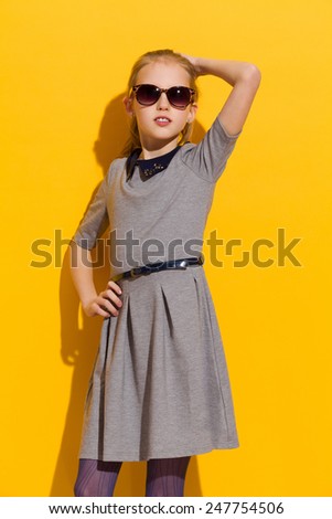 Young girl in sunglasses and gray dress posing in the sunlight. Three quarter length studio shot on yellow background