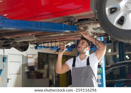 Car chassis inspection. Focused mechanic standing under car holding lamp and checking a chassis