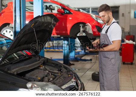 Focused auto mechanic working on a computer connected to a car engine