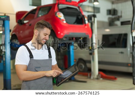 Mechanic using a digital tablet. Smiling man in workshop pointing at a digital tablet.