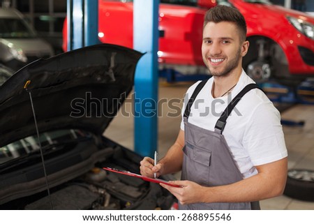 Car service inventory. Smiling mechanic in auto repair shop makes a note on a clipboard