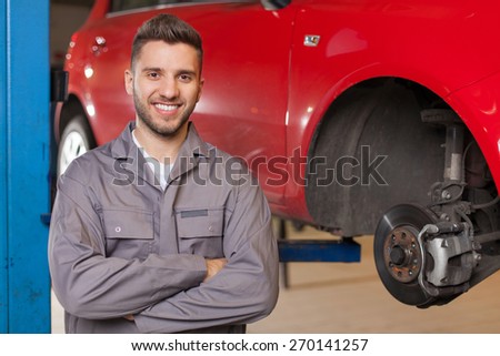 Smiling man in workshop posing with arms crossed against red car at the lift.
