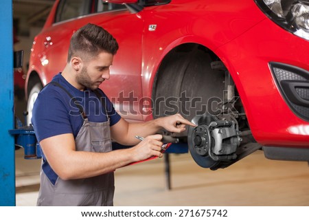 You should change this car part. Mechanic holding a clipboard and pointing at car brakes in auto repair shop. Waist up shot in auto repair shop.