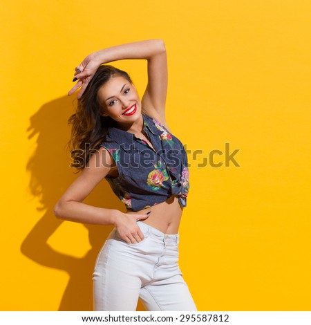 Happy  young woman posing with arm raised over head. Three quarter length studio shot on yellow background.
