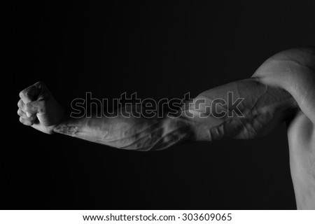 Strong Arm. Close up of  man\'s muscular arm and fist. Black and white studio shot on black background.