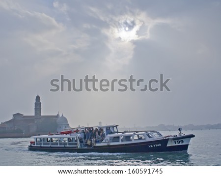 VENICE - OCTOBER 26, 2013 - A water bus or vaporetto full of tourists sets sail during a cloudy autumn in Venice.