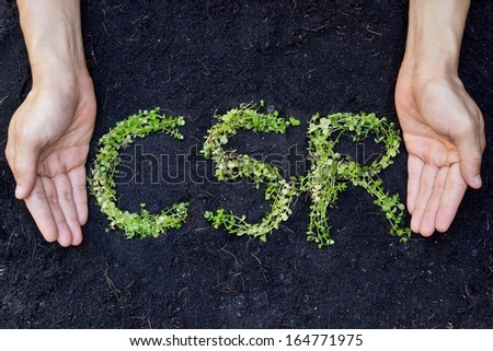 small green plants arranged in csr shape with supporting hands on soil background - corporate social responsibility