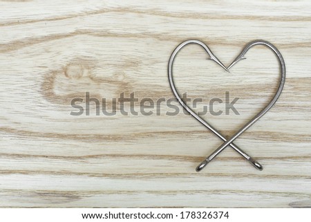 fish hook arranged as a heart shape on wood texture / heart shaped fish hook on wood background