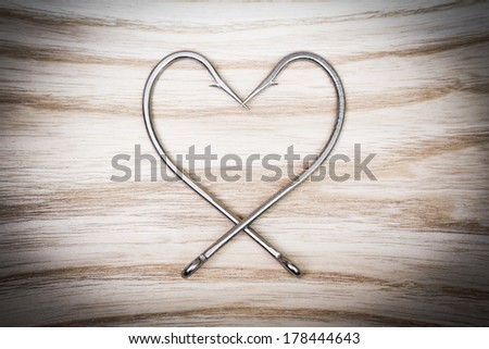 fish hook arranged as a heart shape on wood background