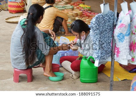 Pakse, Laos - March 26, 2013: A Laotian woman was providing a nail spa to a female customer on the footpath in front of Dao Ruang Market.