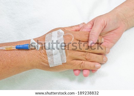 old hands holding each other with IV solution in a patient\'s hand