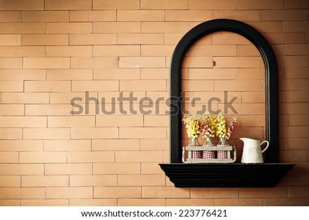 black wooden shelf on orange brick wall with a white jug and bottles of flowers