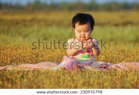Asian baby girl playing and sitting on the cloth in the yellow grass flower field