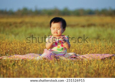 Asian baby girl playing and sitting on the cloth in the yellow grass flower field