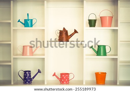 colorful gardening tools on white shelf - bucket, watering can