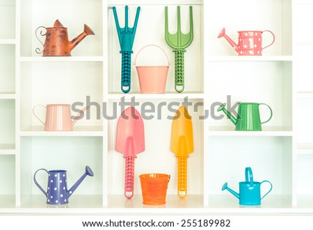 colorful gardening tools on white shelf - fork, shovel, rake, bucket, watering can