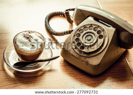A cup of cappuccino coffee on wooden table with old telephone