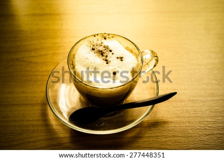 A cup of cappuccino coffee on wooden table with morning light