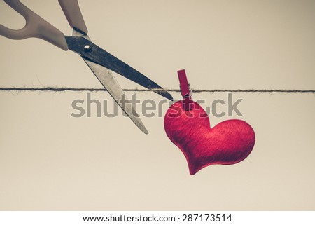 Scissors cutting a rope with a red heart - Broken heart concept